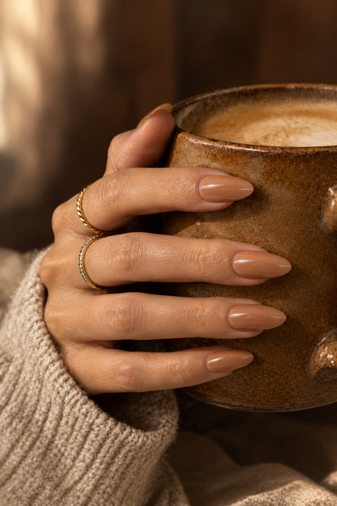 Glossy caramel nude almond acrylic nails holding a ceramic coffee cup.