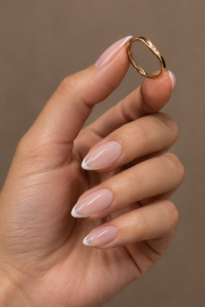Short almond acrylic nails with sheer pink polish and thin ivory French tips.